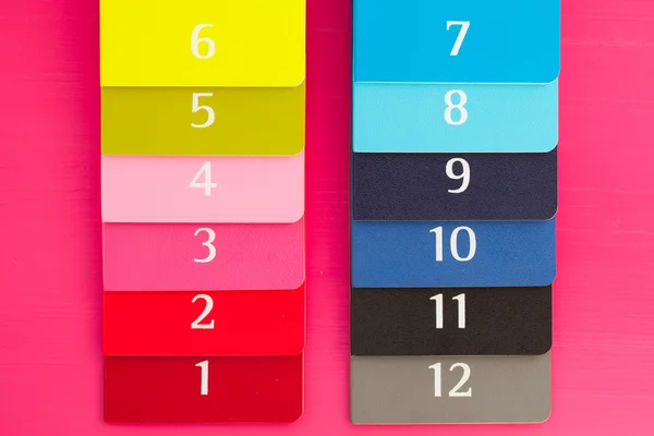 Tizenkét különböző színű naplók egy rózsaszín fa íróasztal — Stock Fotó