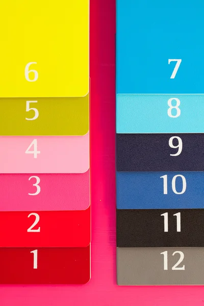 Dwanaście pamiętniki inny kolor na różowy biurko z drewna — Zdjęcie stockowe