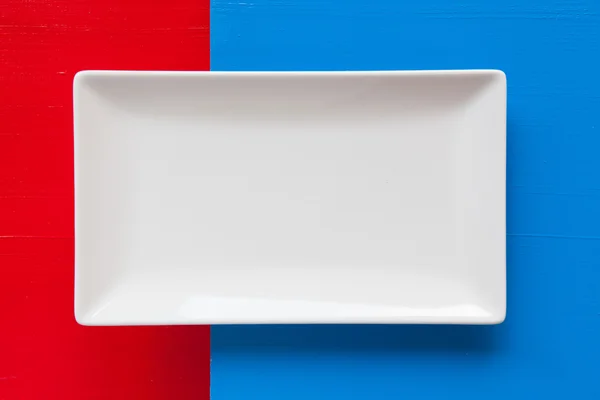 Prato de cerâmica branca vazia sobre fundo azul e vermelho — Fotografia de Stock
