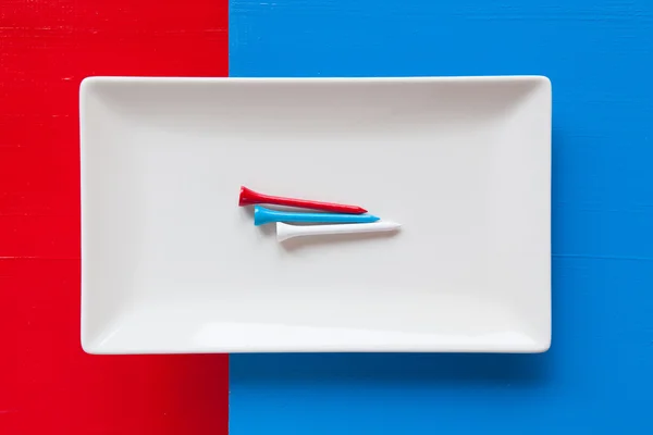 Pusty biały ceramicznych danie z golf skarpety na nad niebieski i czerwony bac — Zdjęcie stockowe