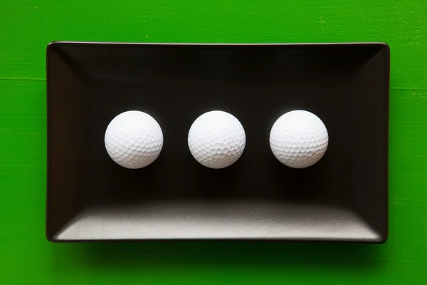 Black ceramic dishes with white golf balls — Stock Photo, Image