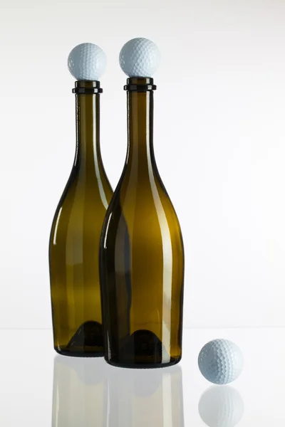 Garrafas de vinho vazias e bolas de golfe em uma mesa de vidro — Fotografia de Stock