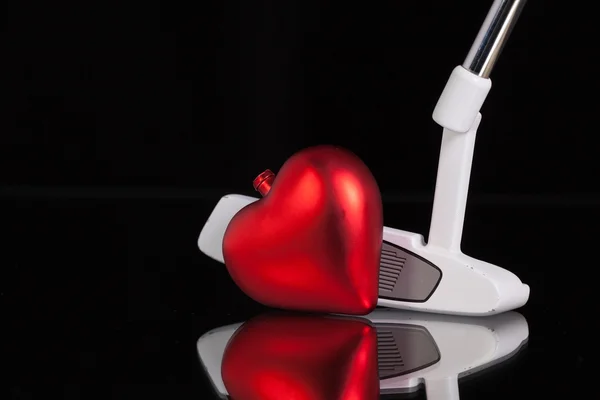 Клюшка для гольфа и символ любви на черном стеклянном столе — стоковое фото