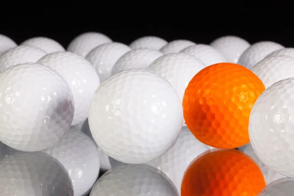 Bola de golfe laranja solitária entre bolas de golfe branco — Fotografia de Stock