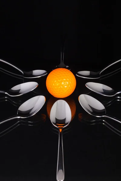 Theelepels en oranje golf ball op de zwarte glazen tafel — Stockfoto