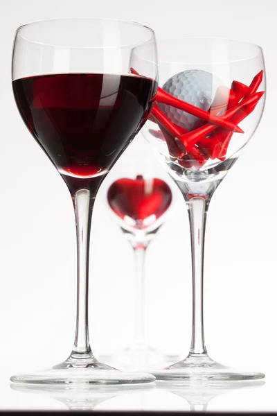 Copas de vino con vino tinto, corazón y pelota de golf — Foto de Stock