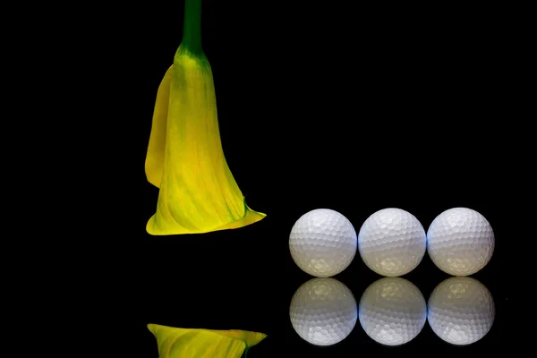 Gelbe Calla-Lilie und Golfball auf schwarzem Glasteller — Stockfoto