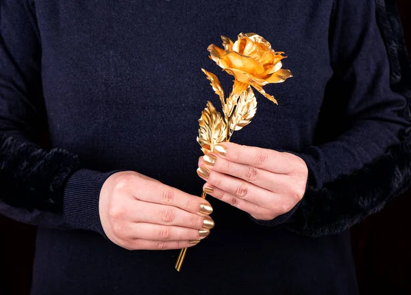 A woman is holding an artificial golden rose. Women\'s hands with trendy gold manicure. Close up.