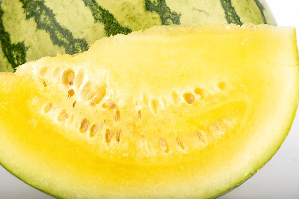 A cut piece of yellow watermelon on a background of watermelon. Food background concept.