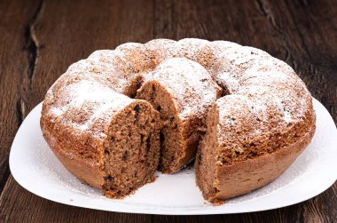 Pudra şekeri serpiştirilmiş halka şeklinde bir kek. Kekin ortasında beyaz bir tabakta dilimle. Ev yapımı kek..