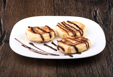 Tahta arka planda beyaz bir tabakta üç peynirli krep. Çikolata soslu peynirli krep..