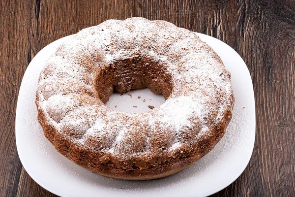 Pudra şekeri serpiştirilmiş halka şeklinde bir kek. Ahşap arka planda beyaz bir tabakta ev yapımı kek..