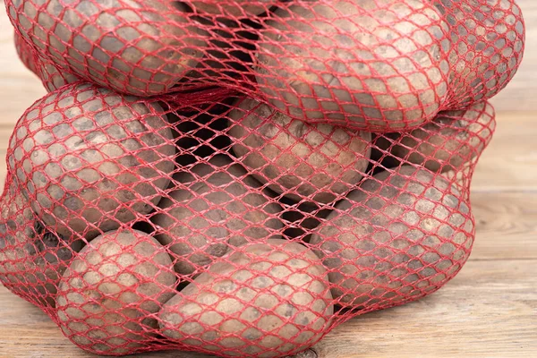 Primer plano de una red roja con patatas sobre un fondo de madera. — Foto de Stock