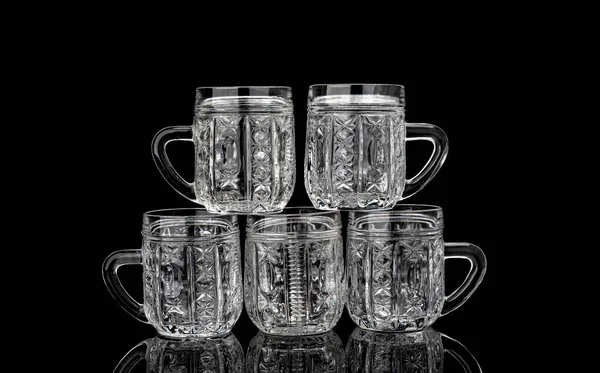 Pyramid of five empty crystal mugs on a black background with reflection. — Stock Photo, Image