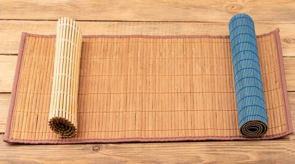 Three food mats on a wooden background. Two mats rolled up. Traditional kitchen utensils.
