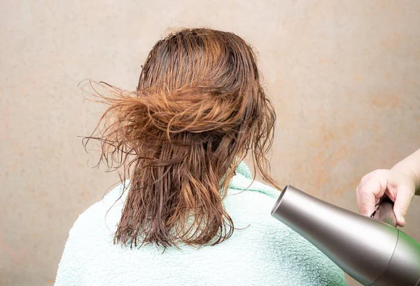 Drying wet hair with an electric hand-held hair dryer. Hair flutters in hot air. Hair care.