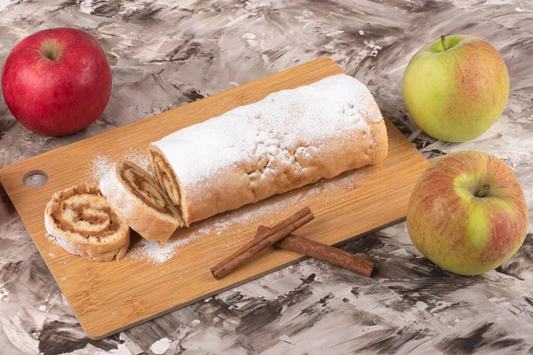 Rolo de maçã ou strudel em uma placa de corte, paus de canela e maçãs frescas. — Fotografia de Stock