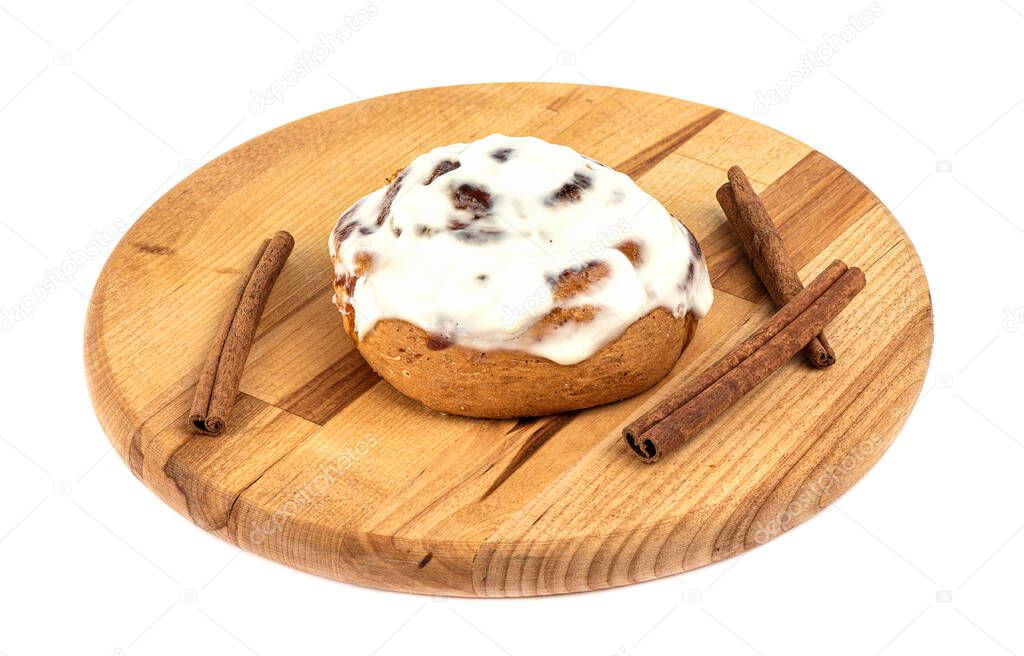 Sugar glazed sweet cinnabon bun on a cutting board over white background. Cinnamon sticks. Homemade buns.