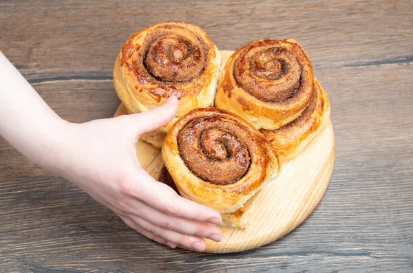 Eine Frauenhand nimmt ein frisch gebackenes Zimtgebäck. — Stockfoto