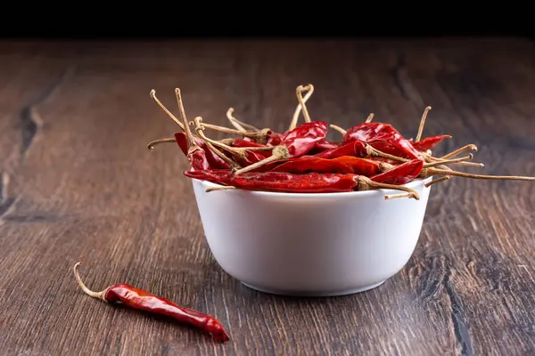 Bowl full of dry hot pepper pods on a wooden background. — Stock Photo, Image