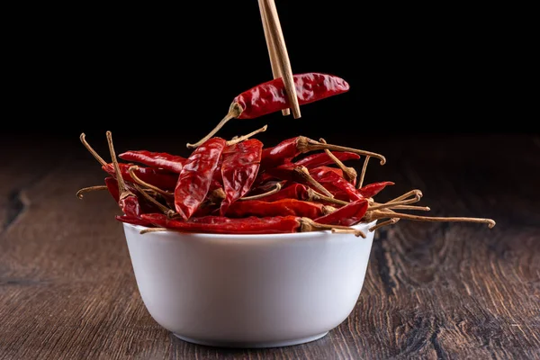 Chopsticks with a pod of hot red pepper over a bowl of pods. — Stock Photo, Image