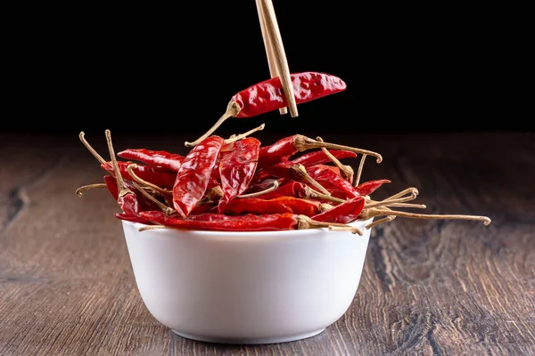 Chopsticks with a pod of hot red pepper over a bowl of pods. — Stock Photo, Image