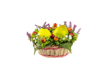Yapay armut ve limon, beyaz arkaplan üzerine hasır bir sepette suni çiçekler arasında..