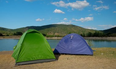 Bir dağ gölünün kıyısındaki çok renkli çadırlar yeşil bir ormanla çevrili erişilemez kayalıklara karşı..
