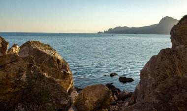Kayalar, ılık bir yaz akşamında gün batımında hafif deniz dalgaları.