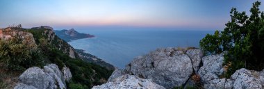 Akdeniz manzarası. Kırım yarımadasının güney kıyısındaki Karadeniz kıyısındaki orman kayaları gün batımında.