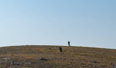 Güneşli bir günde yüksek bir tepenin zirvesine koşan genç bir adamın silueti..