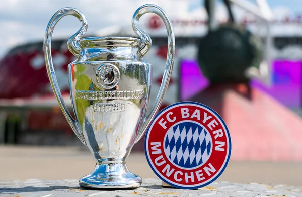 14 Haziran 2021 Münih, Almanya. FC Bayern Münih futbol kulübü ve UEFA Şampiyonlar Ligi Kupası 'nın amblemi modern bir stadyumun arka planına karşıdır..