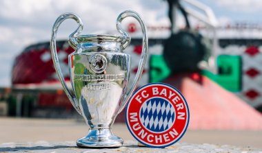 14 Haziran 2021 Münih, Almanya. FC Bayern Münih futbol kulübü ve UEFA Şampiyonlar Ligi Kupası 'nın amblemi modern bir stadyumun arka planına karşıdır..