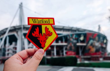 30 Ağustos 2021, Watford, İngiltere. Watford F.C. Modern bir stadyumun arka planına karşı futbol kulübü amblemi..