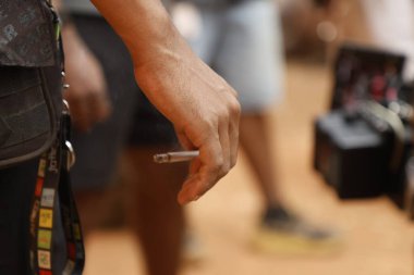 Yakından bakınca, elinde yanan bir sigara tutan bir erkek eli görülüyor.