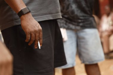 Yakından bakınca, elinde yanan bir sigara tutan bir erkek eli görülüyor.