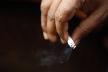 Yakından bakınca, elinde yanan bir sigara tutan bir erkek eli görülüyor.