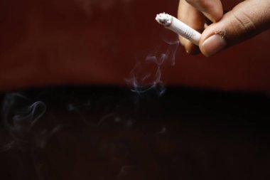 Yakından bakınca, elinde yanan bir sigara tutan bir erkek eli görülüyor.