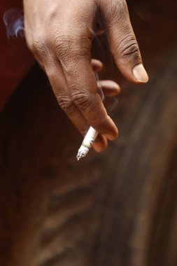 Yakından bakınca, elinde yanan bir sigara tutan bir erkek eli görülüyor.