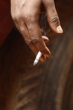 Yakından bakınca, elinde yanan bir sigara tutan bir erkek eli görülüyor.
