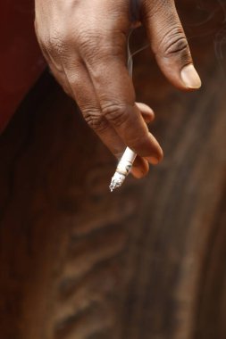 Yakından bakınca, elinde yanan bir sigara tutan bir erkek eli görülüyor.
