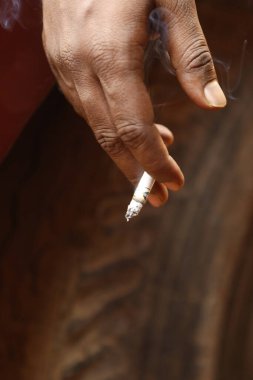 Yakından bakınca, elinde yanan bir sigara tutan bir erkek eli görülüyor.