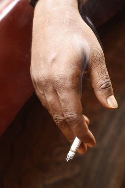 Yakından bakınca, elinde yanan bir sigara tutan bir erkek eli görülüyor.