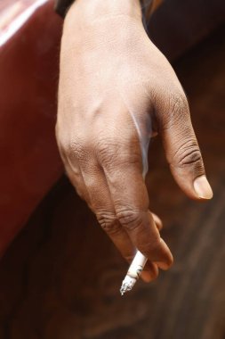 Yakından bakınca, elinde yanan bir sigara tutan bir erkek eli görülüyor.