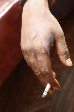 Yakından bakınca, elinde yanan bir sigara tutan bir erkek eli görülüyor.