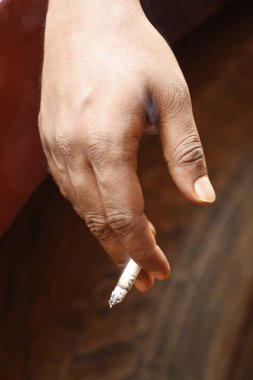 Yakından bakınca, elinde yanan bir sigara tutan bir erkek eli görülüyor.