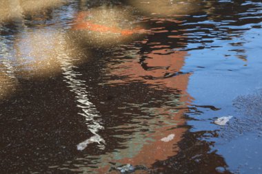 Yağmurlu bir yolda yansıtılan bir binanın yansıması.