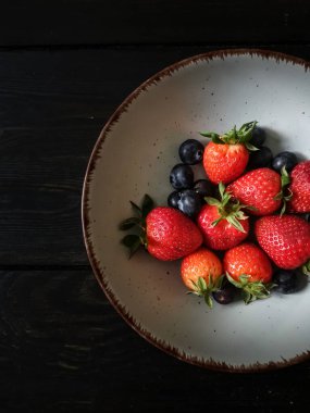 Parlak tabakta taze çilek ve yabanmersini.