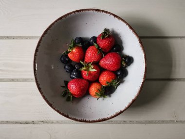 Parlak tabakta taze çilek ve yabanmersini.