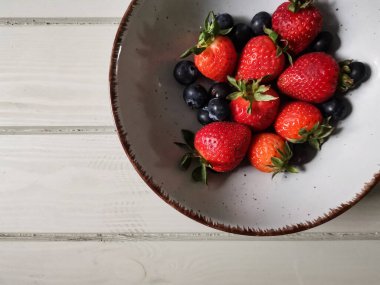 Parlak tabakta taze çilek ve yabanmersini.